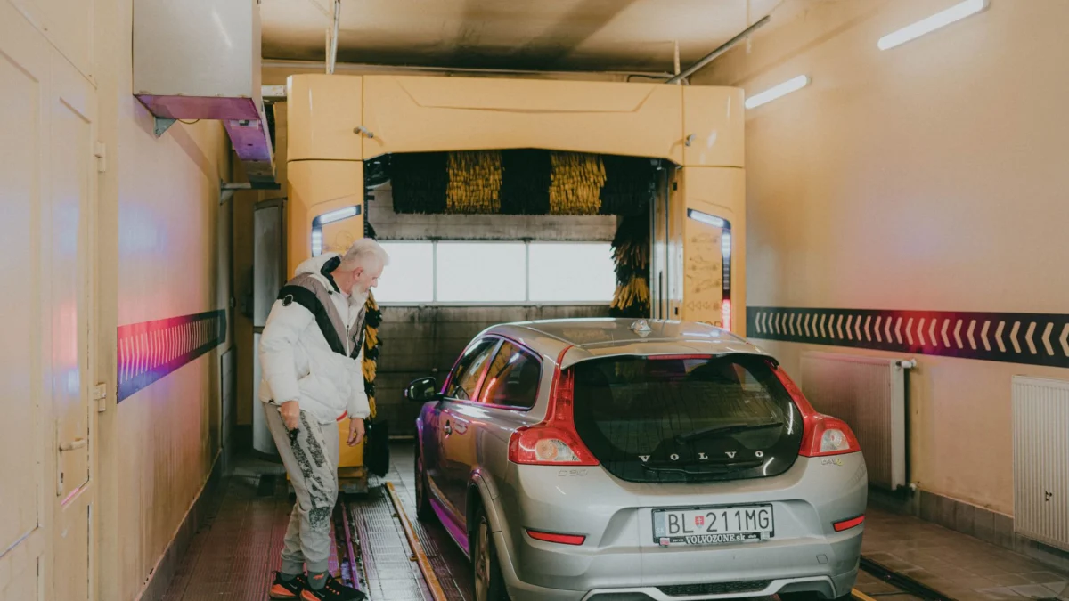 Een zilveren Volvo V40 in een automatische wasstraat met een man die in de buurt kijkt.