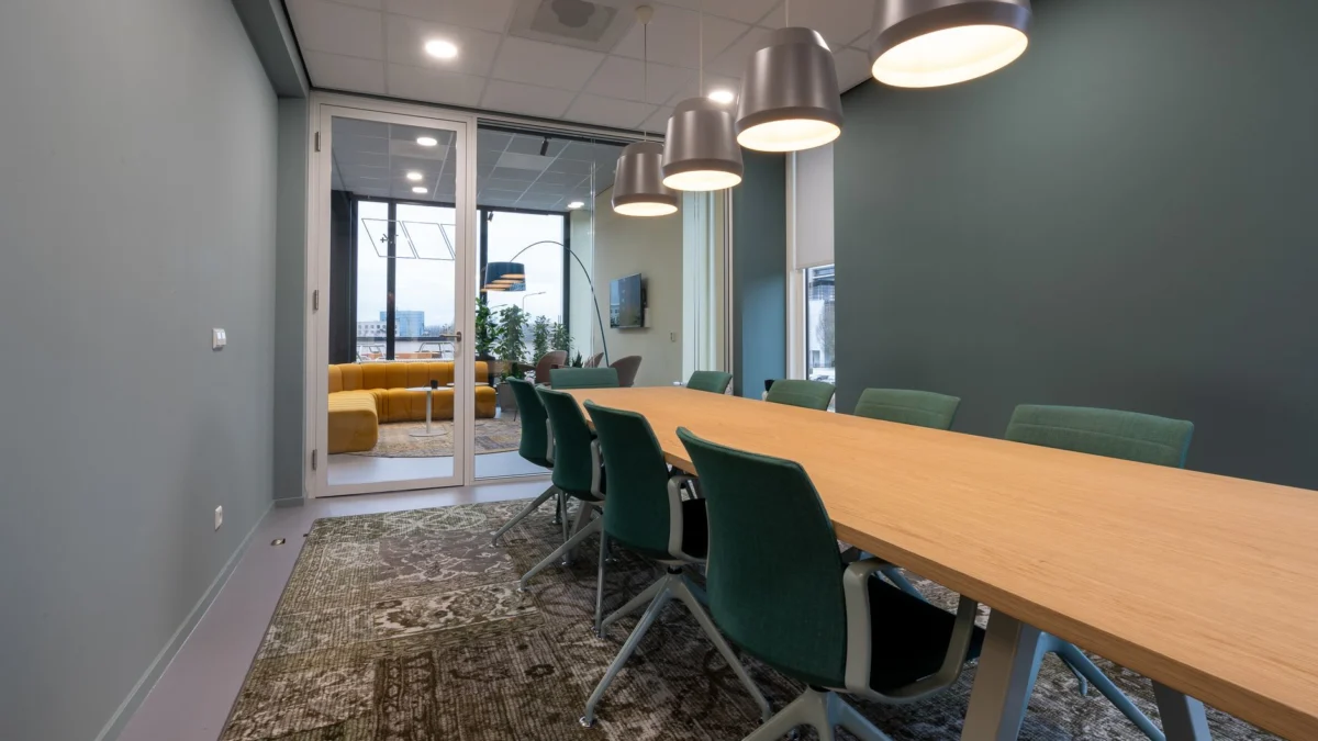 Ruime vergaderzaal met een eigentijdse uitstraling, met een lange tafel, stoelen en hanglampen.