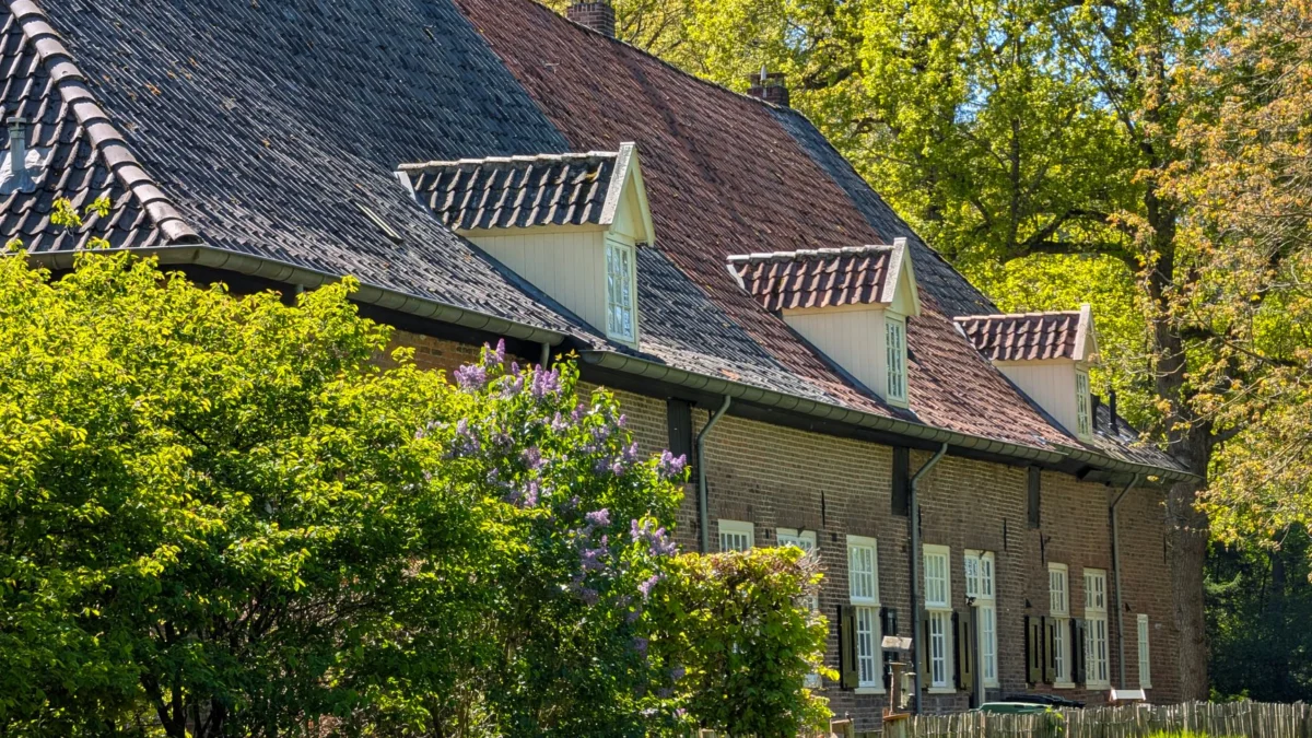 Een schilderachtig uitzicht op een traditionele Hollandse boerderij, omgeven door weelderig groen, kleurrijke bloemen en een zonnige lentestemming.