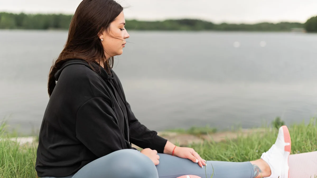 Vrouw die buiten mediteert aan een rustig meer, bevorderend voor gezondheid en welzijn.