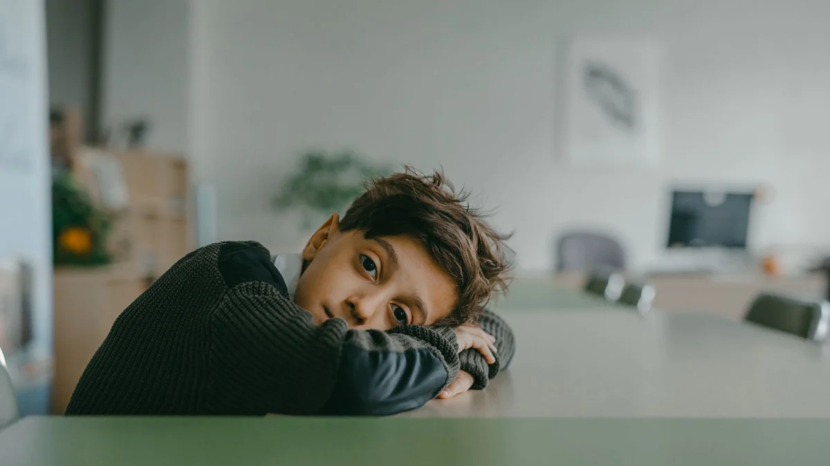 Een nadenkende jongen leunt op een bureau in een rustige klasomgeving.