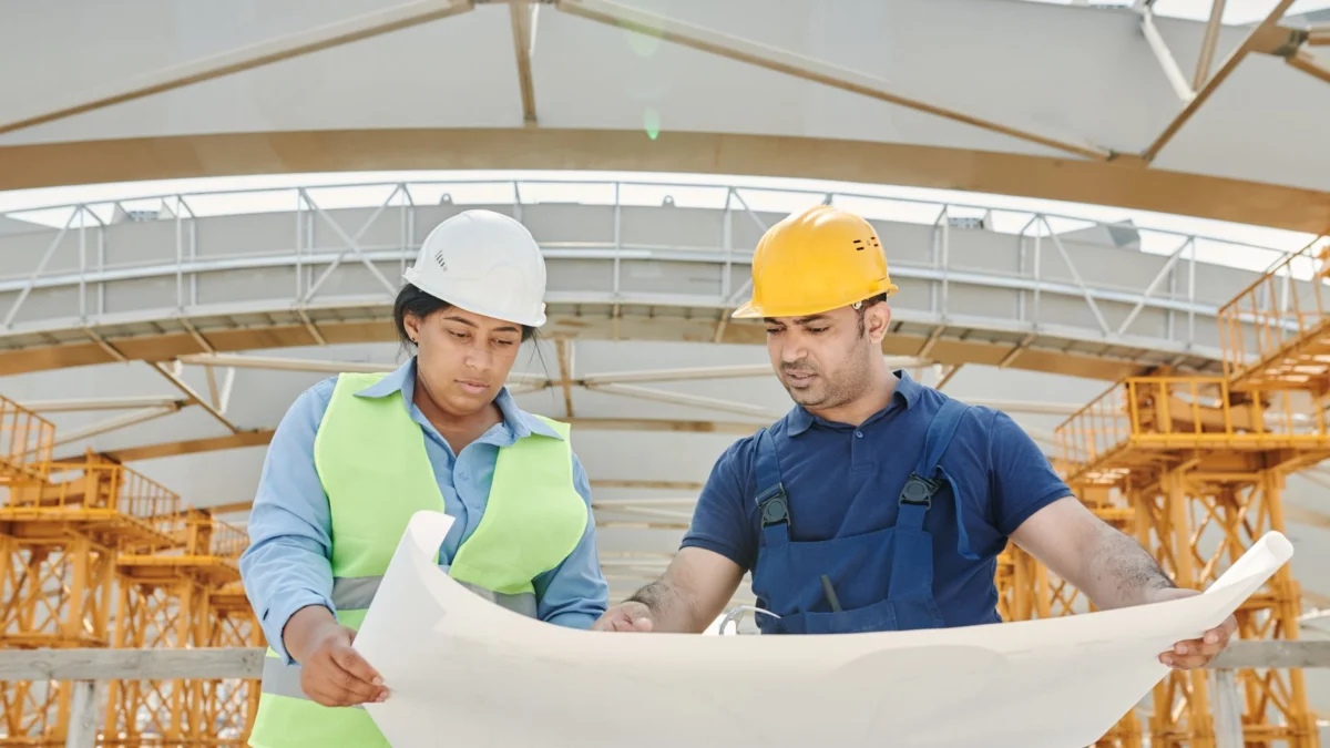 Mannelijke en vrouwelijke ingenieurs die blauwdrukken bespreken op een bouwplaats, bevorderen teamwork en planning.