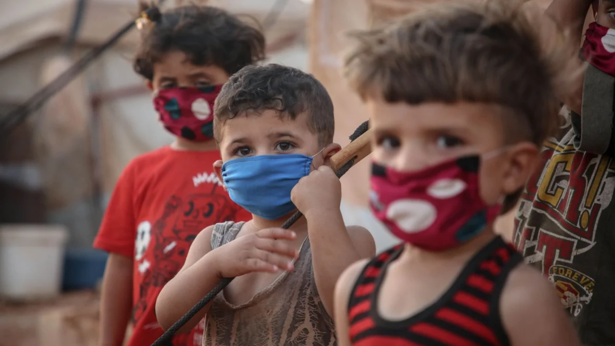 Jonge kinderen dragen mondkapjes in een Syrisch vluchtelingenkamp, wat de impact van de pandemie illustreert.