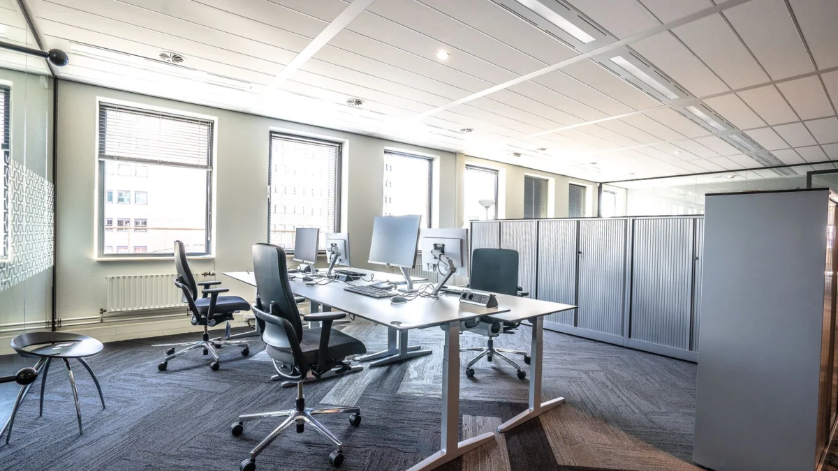 Helder en ruim modern kantoorinterieur met strakke werkplekken en ergonomische stoelen.