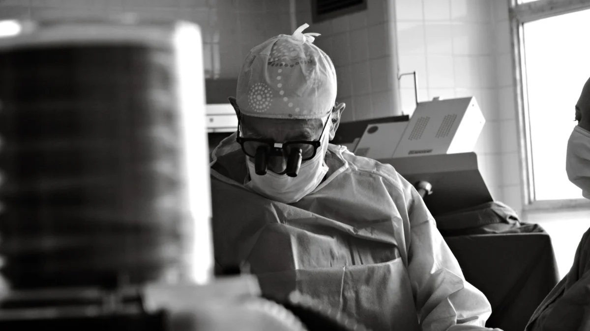 Een chirurg gefocust op een procedure in een operatiekamer van het ziekenhuis, vastgelegd in zwart-wit.