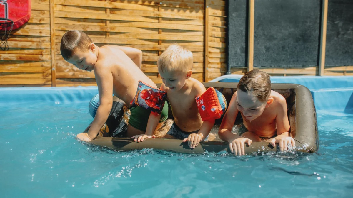 Drie kinderen spelen op een zonnige zomerdag in een zwembad met opblaasbaar speelgoed.