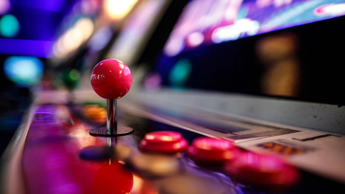 Close-up van een levendige retro arcade-joystick en knoppen met wazige lampjes op de achtergrond.