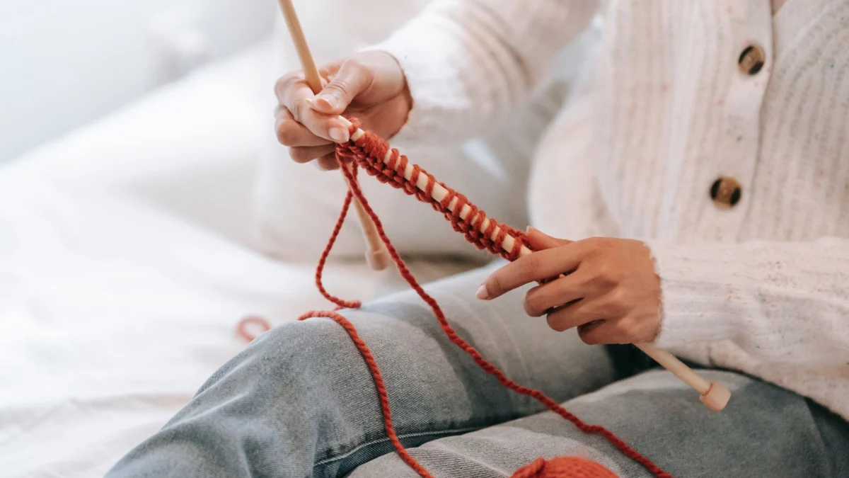 Een vrouw die rode garen breit in een gezellige binnenomgeving, perfect voor ambachtelijke inspiratie.