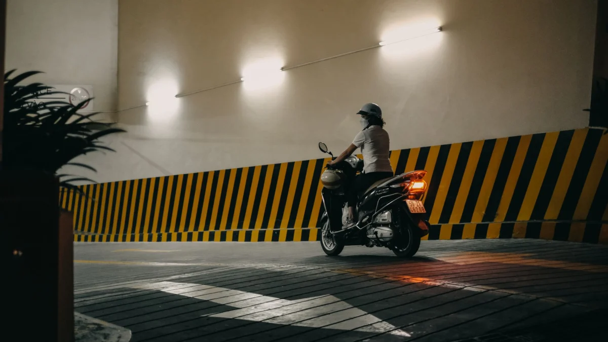 Een persoon op een motorfiets rijdt door een dimme binnenparkeerplaats met reflecterend licht.