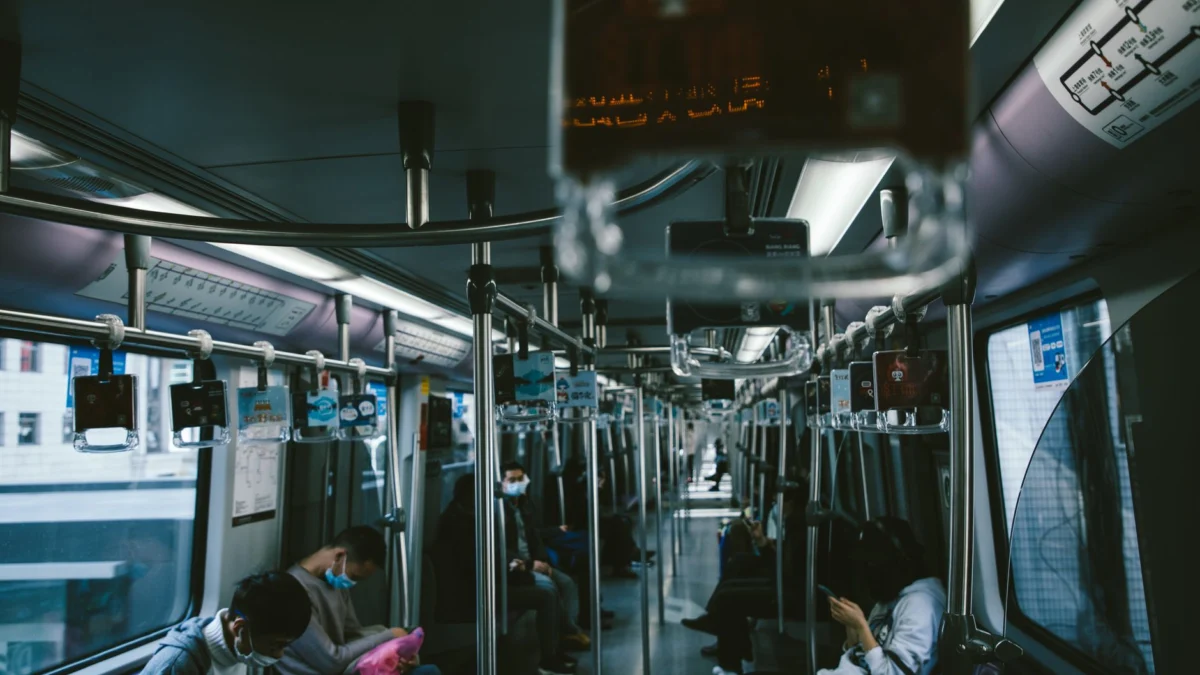 Een rustige scène van gemaskerde forenzen die binnenin een moderne metro zitten en sociale afstand houden.