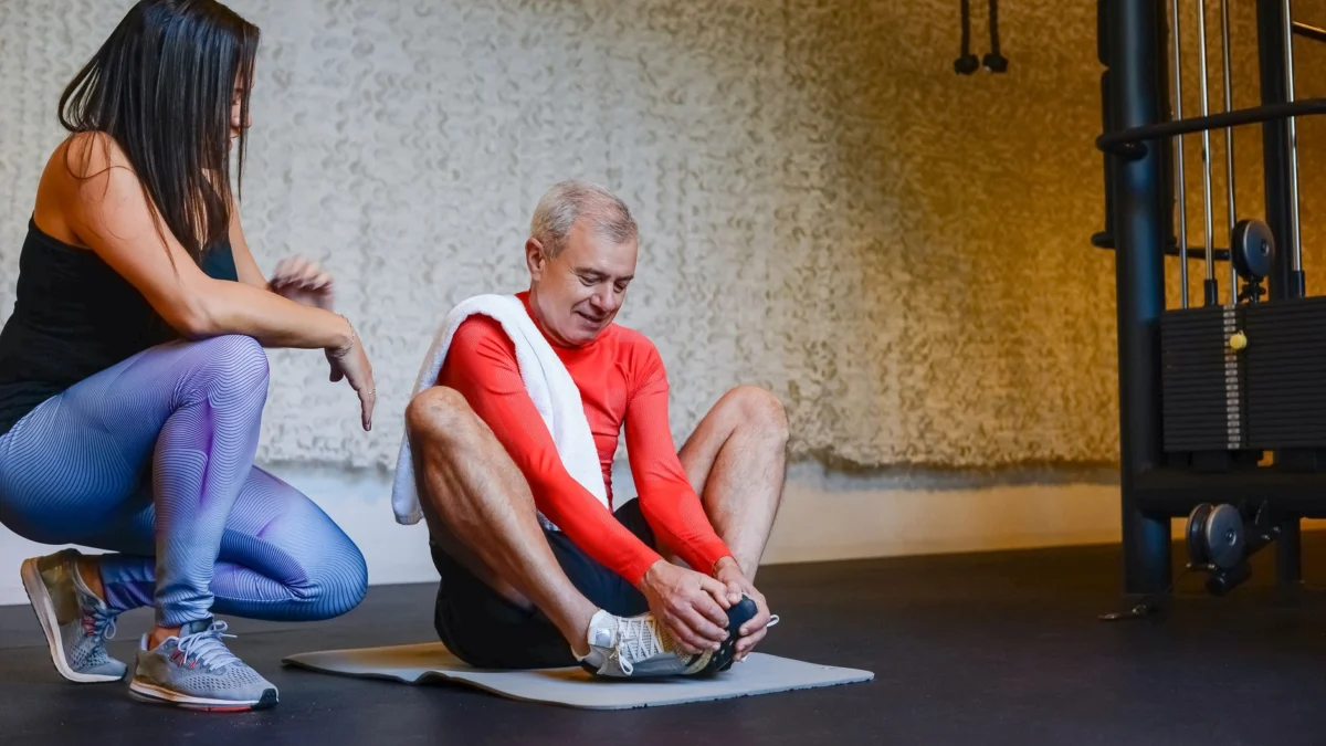 Oudere man strekt zich uit op een yogamat met coach in de sportschool voor een gezonde levensstijl.