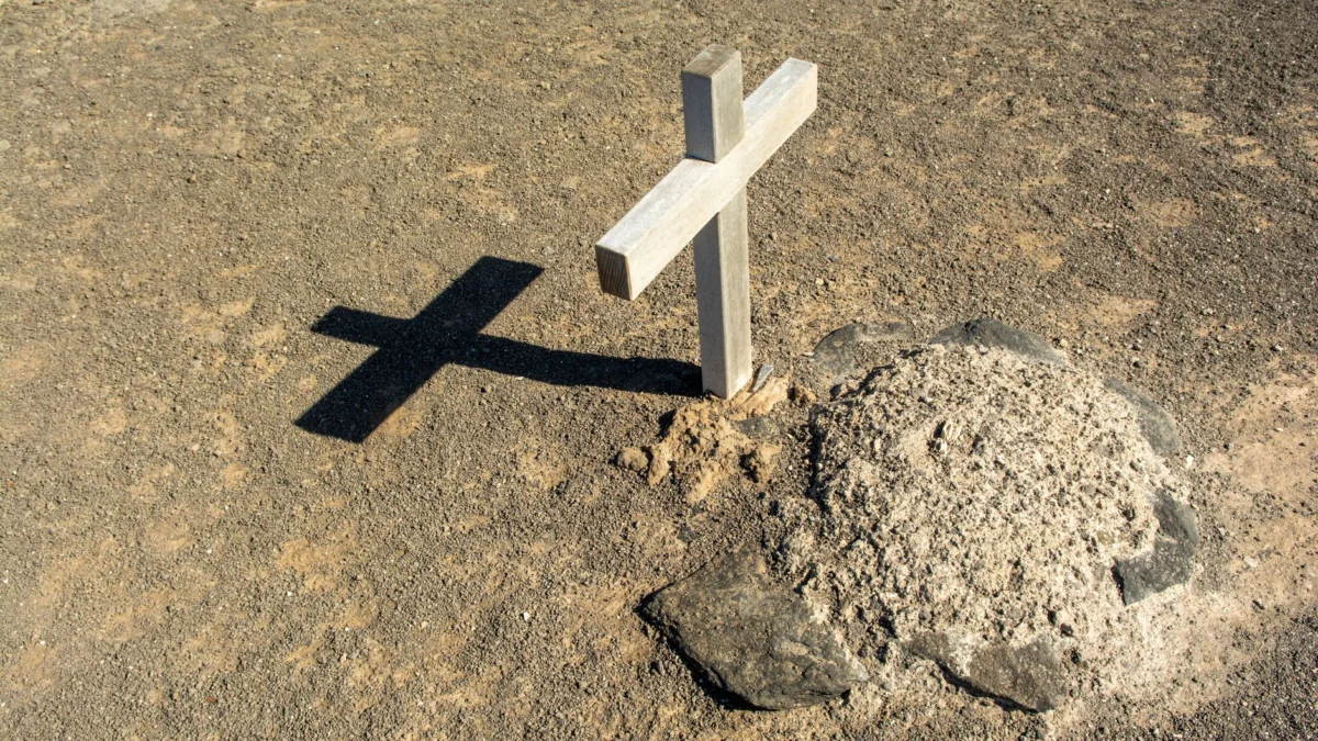 Een eenzame houten kruis dat een schaduw werpt op een dor graf, symbool voor eenzaamheid en spiritualiteit.