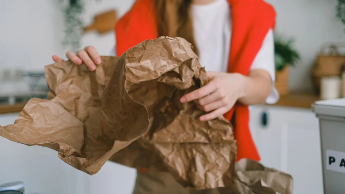 Jonge vrouw sorteert gekreukt papier voor recycling in haar keuken om milieuvriendelijke praktijken te bevorderen.