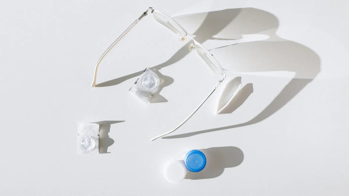 Flat lay van een bril, contactlenzen en een etui op een witte achtergrond, met nadruk op oogzorg.